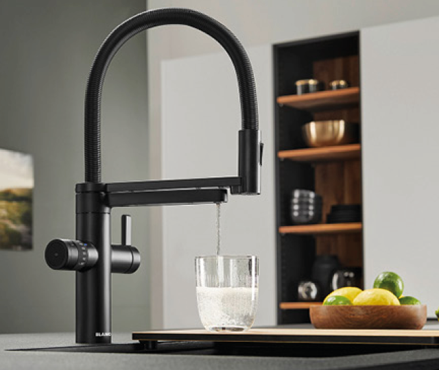 Schwarze Design Küchenarmatur mit flexiblem Auslauf füllt ein Glas mit Wasser. Moderne Spüle mit Obstschale im Hintergrund. Hochwertige Armatur für moderne Küchenplanung.