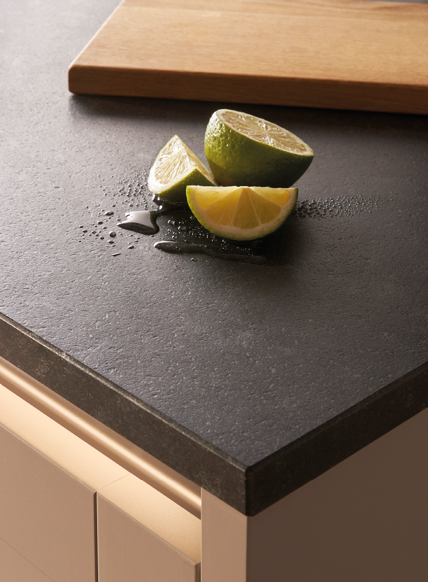 Dunkle Küchenarbeitsplatte mit geschnittenen Limetten und Wassertropfen. Robuste Arbeitsfläche aus Stein oder Keramik für moderne Küchen.