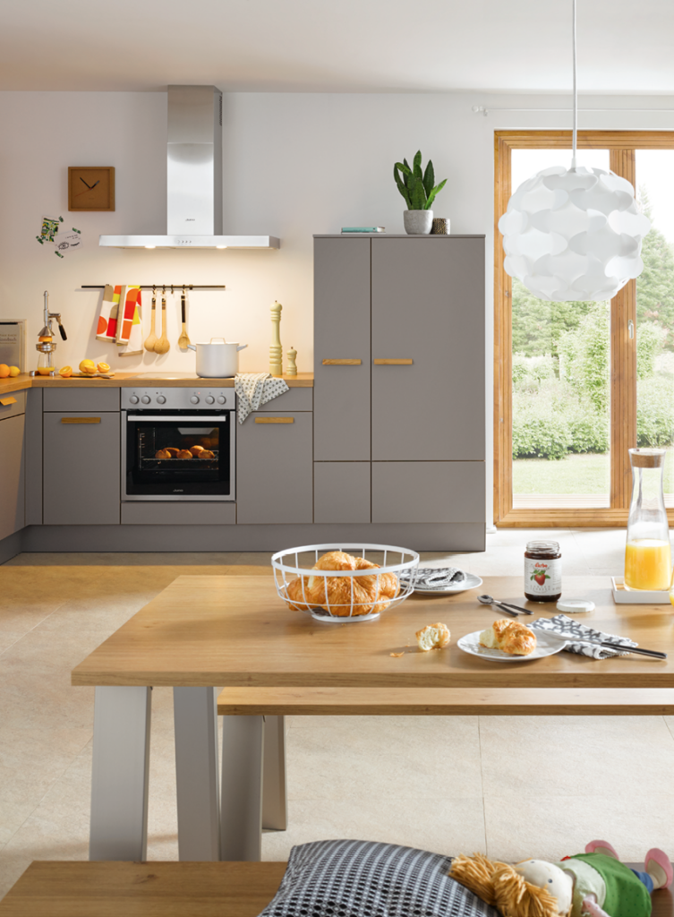 Helle moderne Ausstellungsküche mit grauen Küchenfronten, Backofen, Dunstabzugshaube und Essbereich mit Holztisch als Beispiel für zeitgemäße Küchenplanung Helle moderne Ausstellungsküche mit grauen Küchenfronten, Backofen, Dunstabzugshaube und Essbereich mit Holztisch als Beispiel für zeitgemäße Küchenplanung