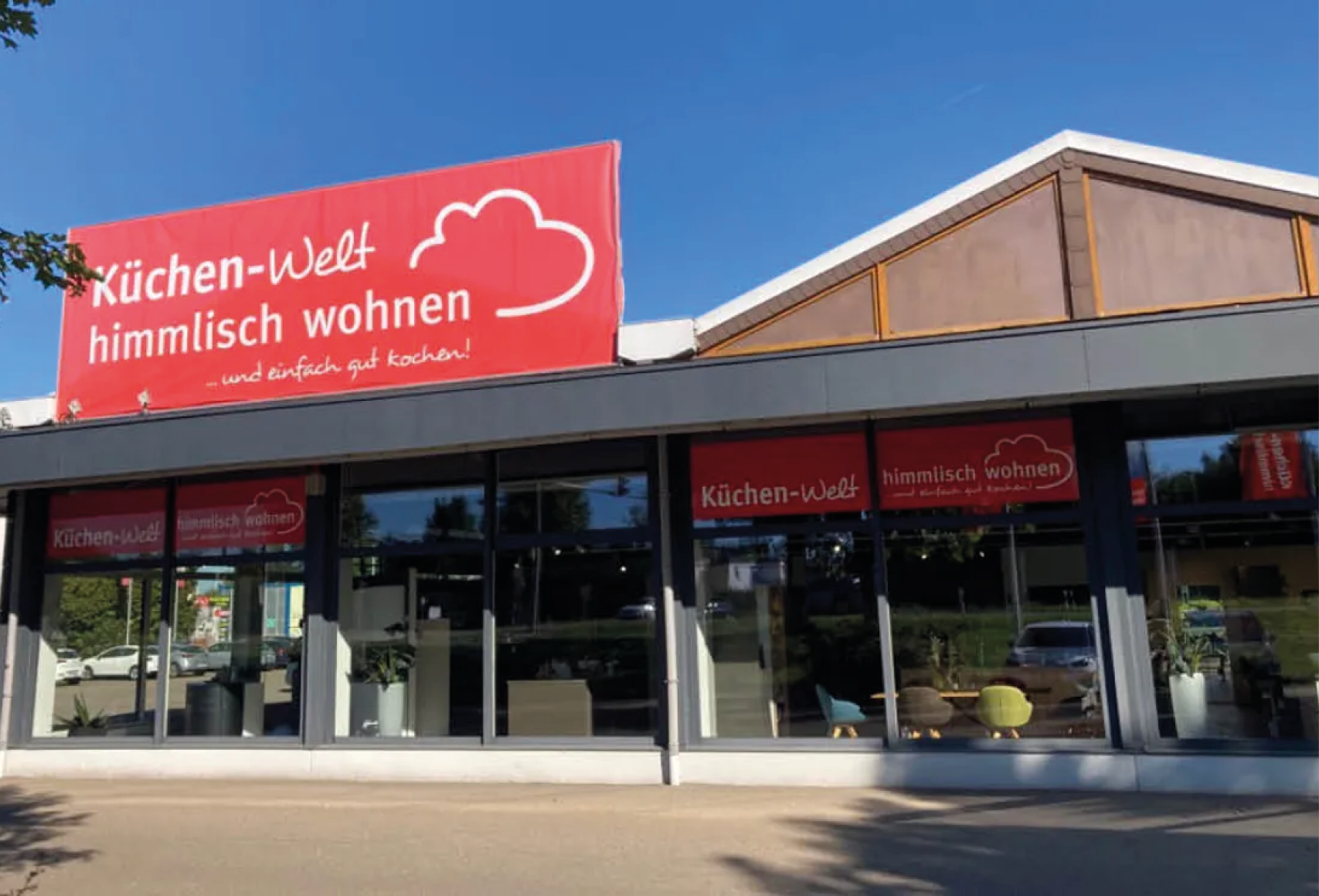 Außenansicht der Küchen Welt himmlisch wohnen in Dillingen mit großer Glasfront und rotem Logo über dem Eingang des Küchenstudios für moderne Küchenplanung und Beratung