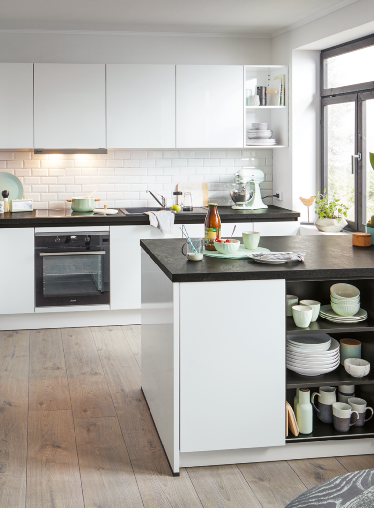 Helle moderne Küche mit weißen Küchenfronten, Kochinsel mit offenen Regalen, schwarzen Arbeitsplatten und integriertem Backofen als Beispiel für zeitgemäße Küchenplanung