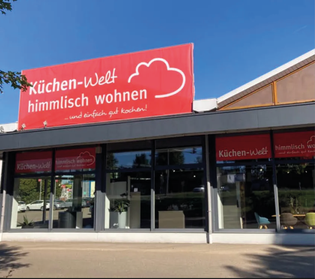 Außenansicht der Küchen Welt himmlisch wohnen in Dillingen mit großer Glasfront und rotem Logo über dem Eingang des Küchenstudios für moderne Küchenplanung und Beratung