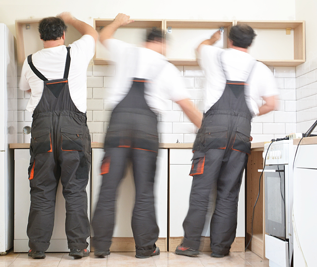Mehrere Küchenmonteure installieren Hängeschränke und montieren eine Küche während der professionellen Küchenmontage im neuen Zuhause