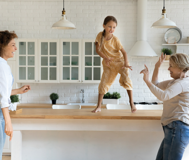 Kind tanzt auf einer Kücheninsel während Familie gemeinsam Zeit in einer hellen modernen Küche verbringt