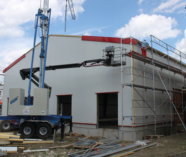 Gebäude im Bau mit Gerüst und Hebebühne, Arbeiter auf Plattform und offener Eingang vorne