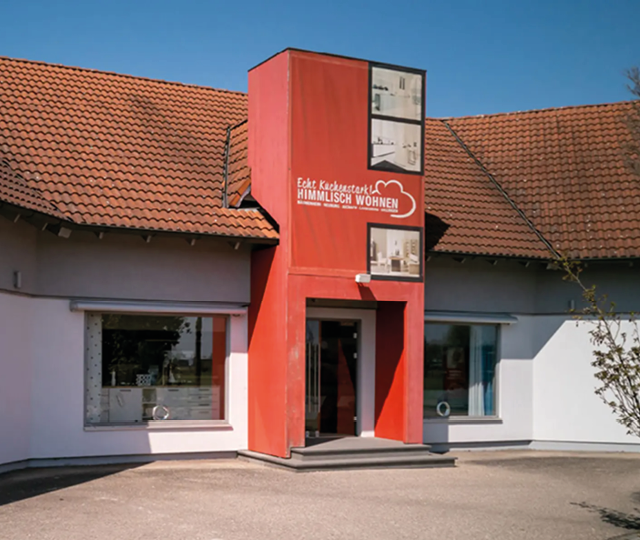 Gebäude mit rotem Eingangsbereich und Schriftzug HIMMLISCH WOHNEN, Fenster links und rechts vom Eingang