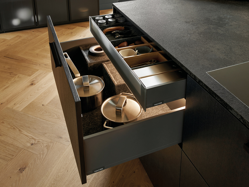 Geöffnete Küchenschubladen mit strukturiertem Stauraum für Töpfe, Gewürze und Küchenutensilien. Hochwertiges Auszugssystem von next125 mit durchdachter Innenorganisation und Beleuchtung.