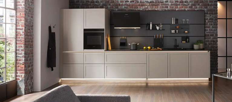 Helle Küchenzeile mit Unterschränken und Arbeitsfläche vor Ziegelwand, schwarze Rückwand mit Regalen und Dunstabzugshaube