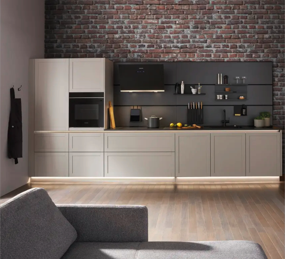 Helle Küchenzeile mit Unterschränken und Arbeitsfläche vor Ziegelwand, schwarze Rückwand mit Regalen und Dunstabzugshaube