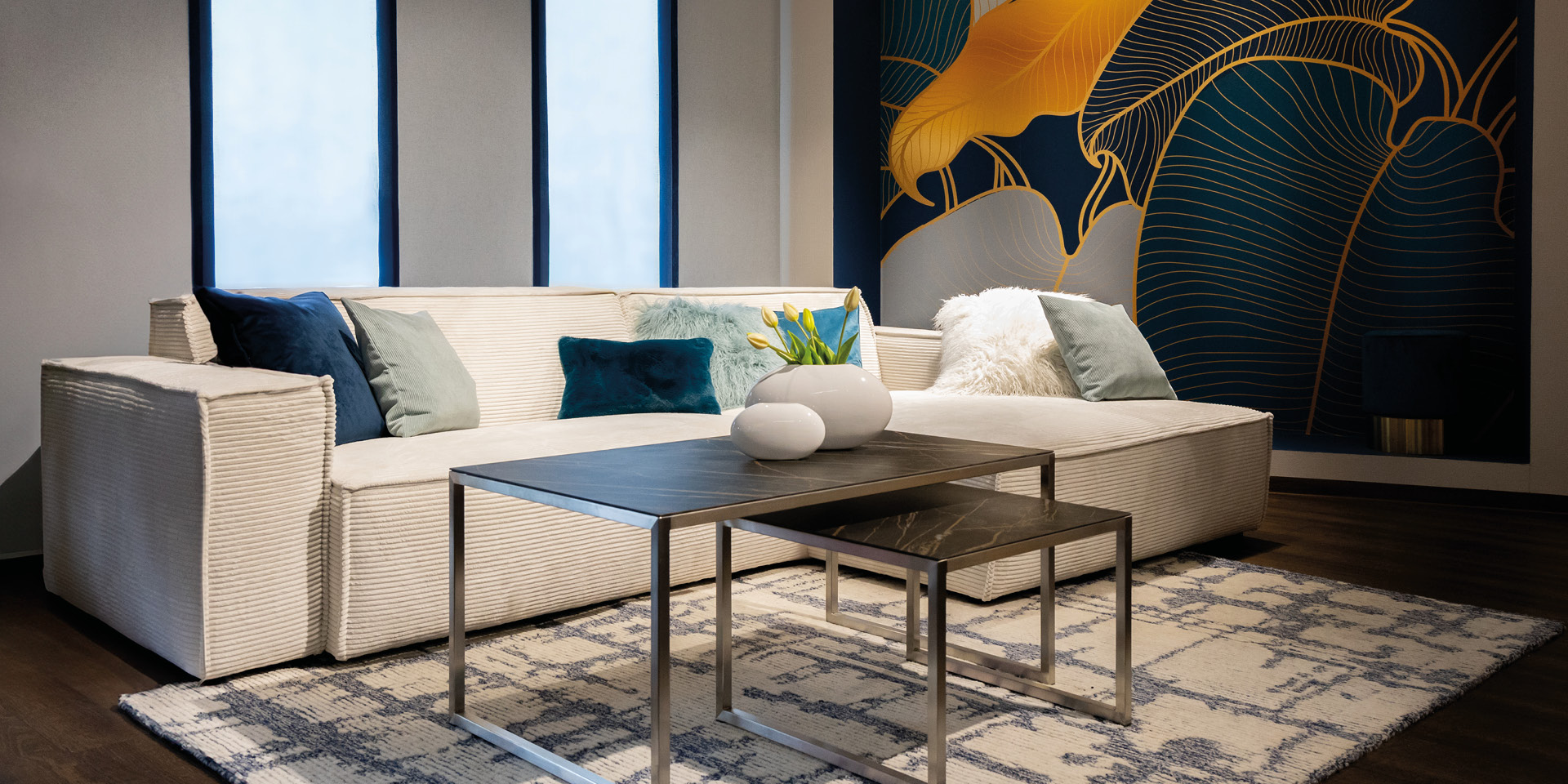 Helles Sofa mit Kissen und Couchtischen vor gemusterter Wand