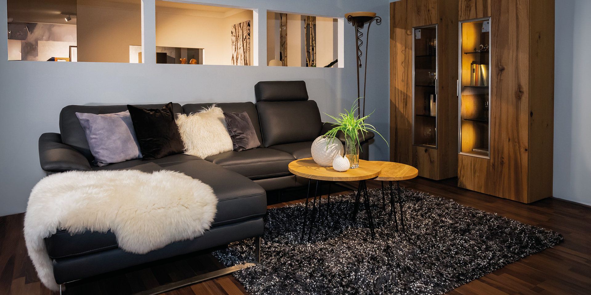 Wohnzimmer mit Ledersofa, Couchtischen und beleuchtetem Vitrinenschrank