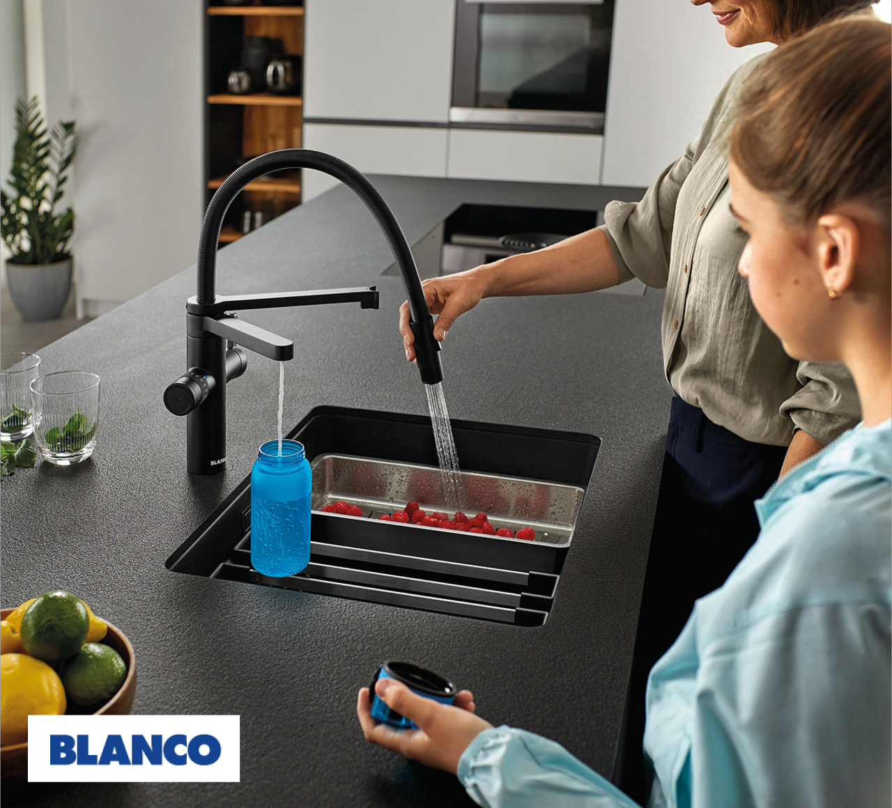 Person hält ausziehbare Küchenarmatur über Spüle, Wasser läuft auf rote Beeren, daneben blaue Flasche, unten links Schriftzug BLANCO