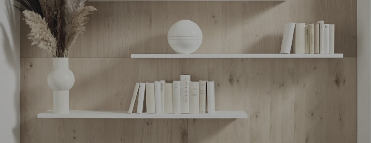 Zwei weiße Wandregale vor Holzrückwand mit Büchern und weißer Vase links, dekorative Kugel mittig