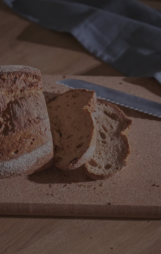 Geschnittenes Brot auf Holzbrett, Messer daneben, dunkler Hintergrund mit Stoff im oberen Bereich