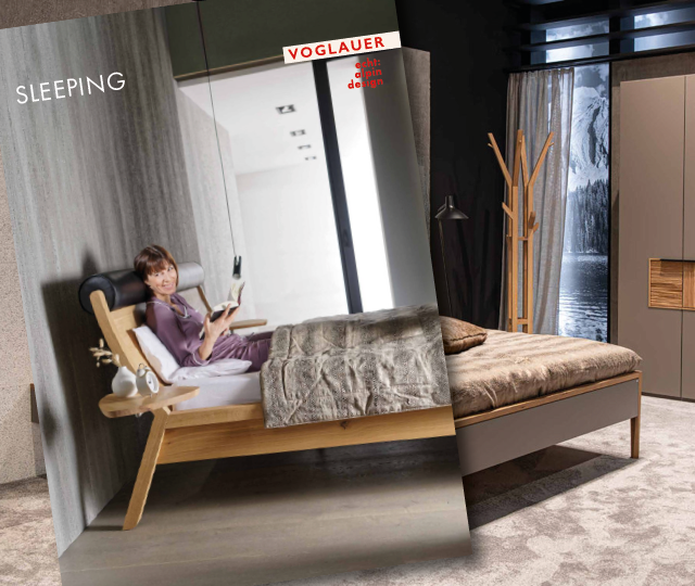 Katalogmotiv mit Schriftzug Sleeping zeigt Person im Bett mit Holzrahmen, dahinter Schlafzimmer mit Kleiderschrank und Garderobe