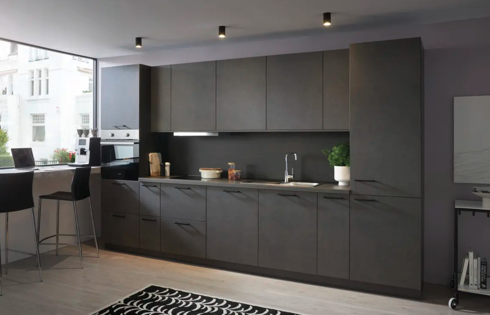 Küchenzeile in dunklen Fronten mit Spüle mittig, Hochschrank links und Bartresen am Fenster mit Hockern