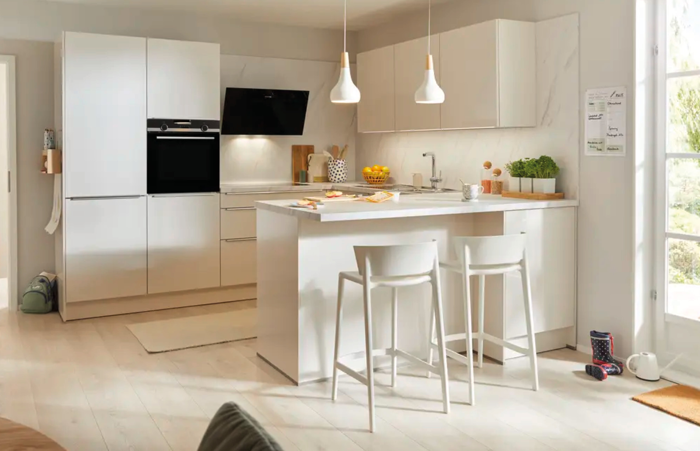 Küche mit heller Insel und zwei Barhockern vorne, Hochschrank links und Hängeschränken hinten