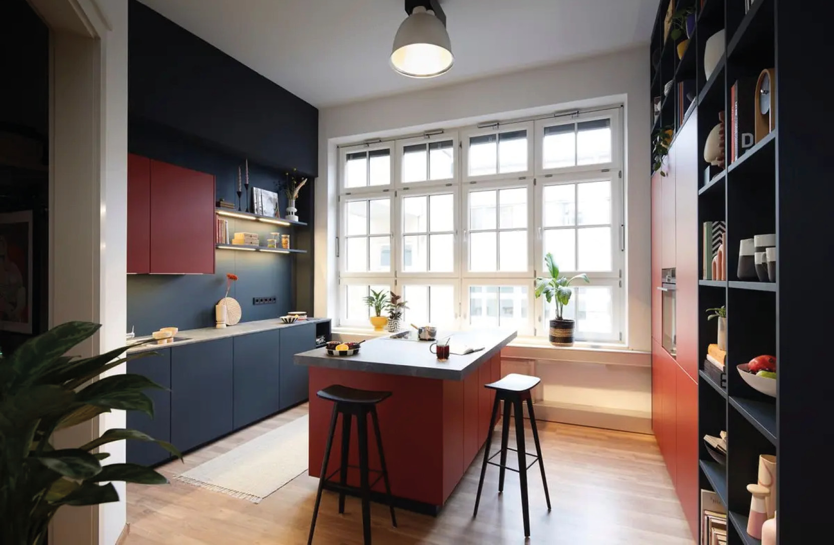 Küche mit roter Insel mittig, dunklen Schränken links und großem Fenster im Hintergrund