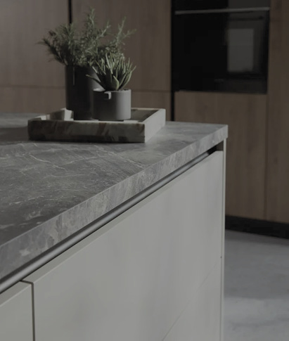 Nahaufnahme einer Kücheninsel mit heller Front und grauer Stein Arbeitsplatte, Tablett mit Pflanze oben