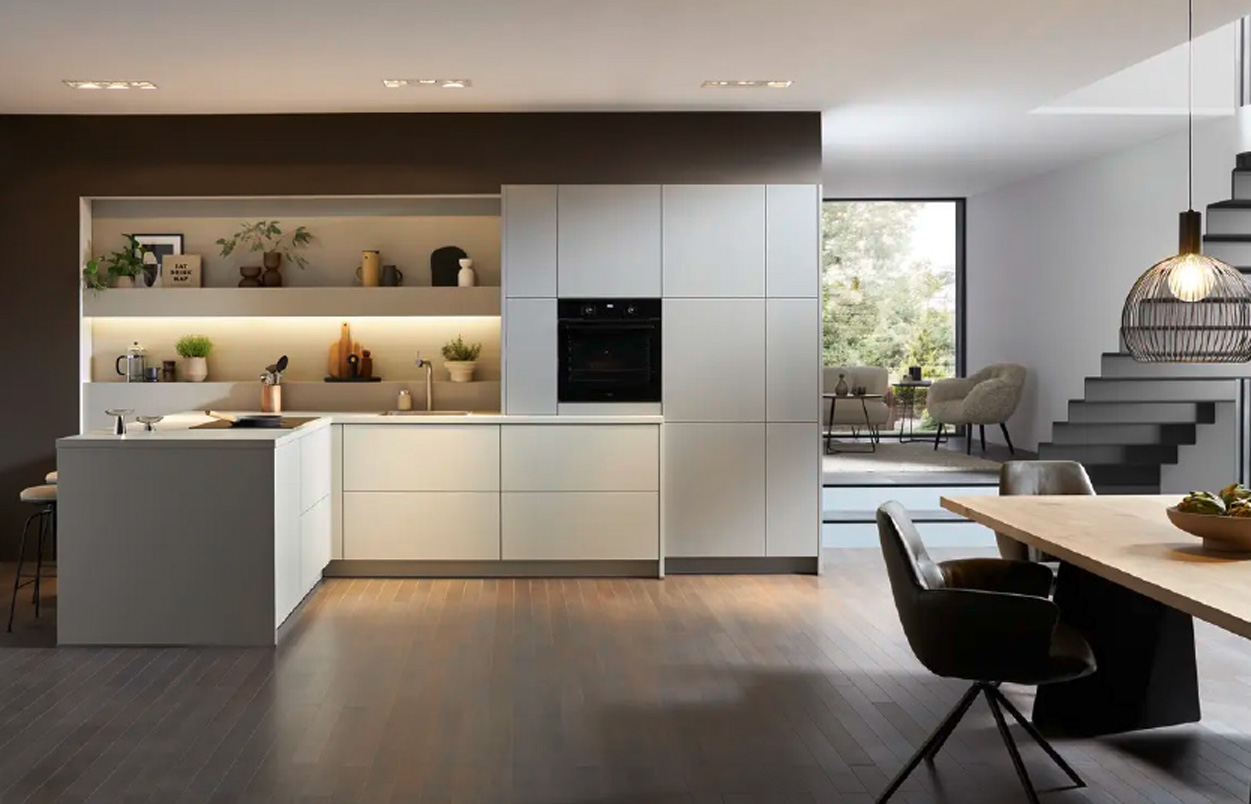 Küche mit heller Insel links, Hochschränken mittig und offenem Wohnbereich rechts mit Treppe und Tisch im Vordergrund