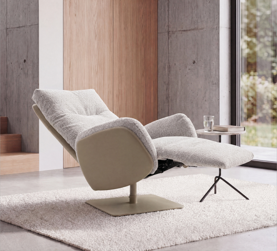 Relaxsessel mit Hocker auf Teppich Heller Relaxsessel mit Hocker, kleinem Tisch und Fensterfront vor Betonwand