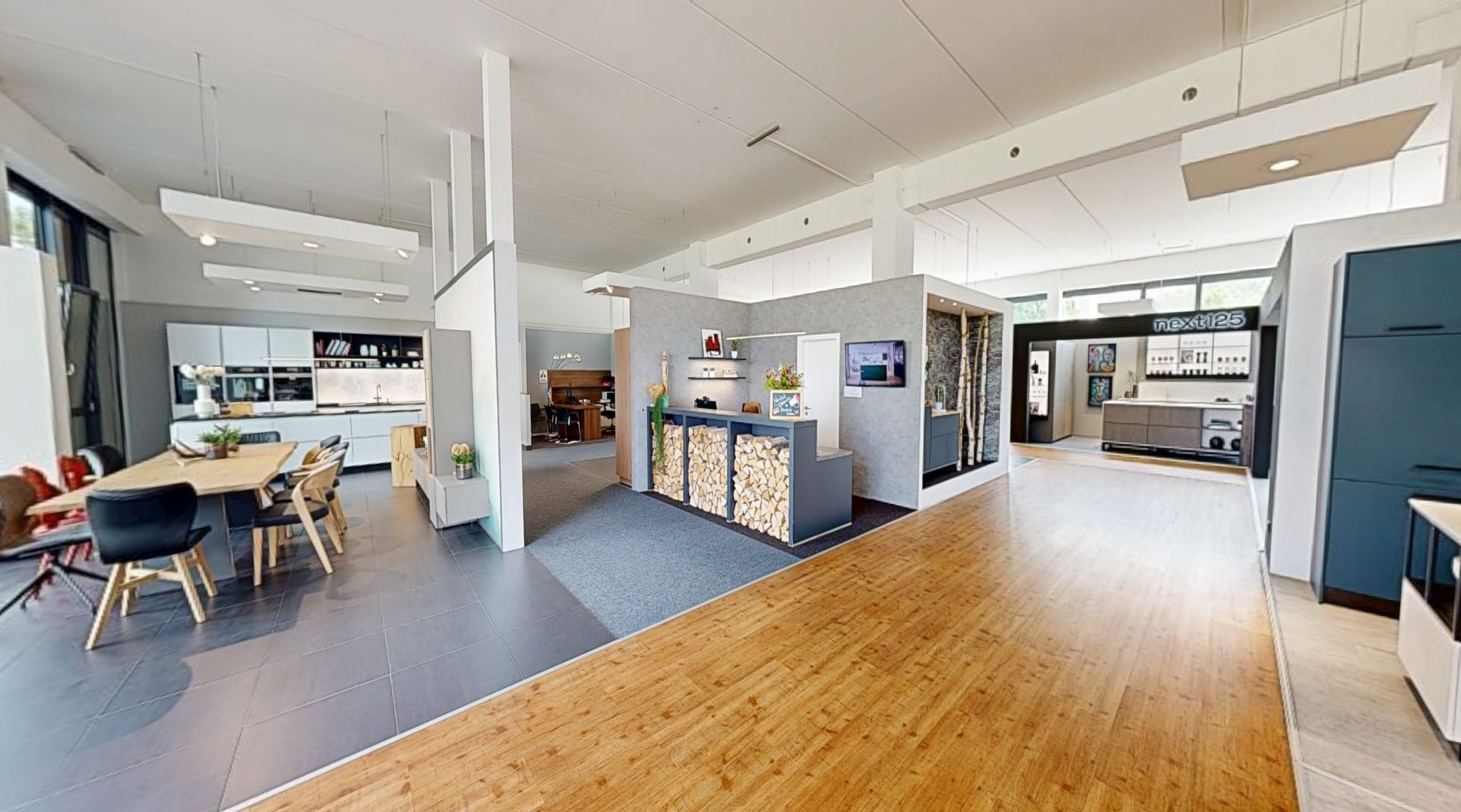 Showroom mit Küchenzeilen, Esstisch, Holzlager und Bereich mit Schriftzug next125